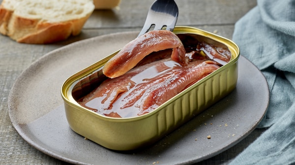 canned anchovy fillets and slices of baguette on wooden kitchen table.