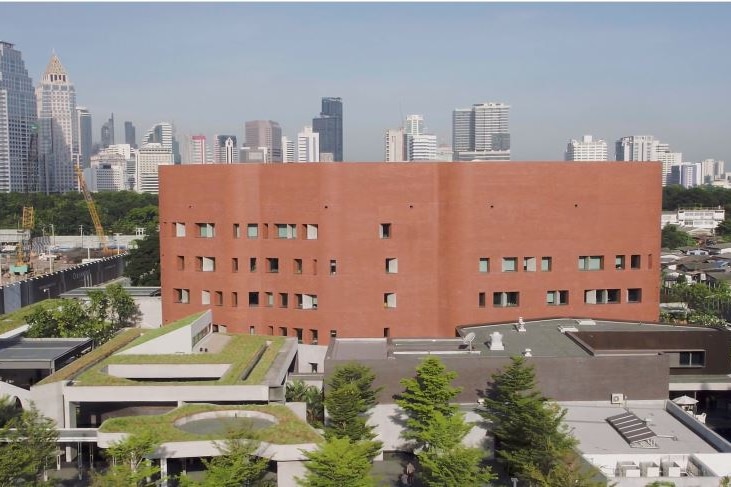 A multi-storey red brick building with Bangkok's skyline in the background.