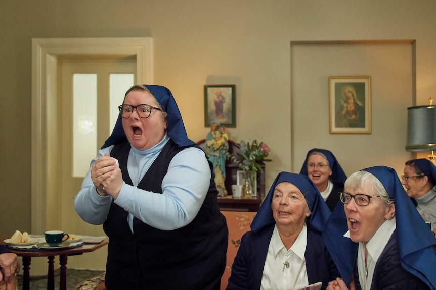 A group of nuns cheer as they watch a television.