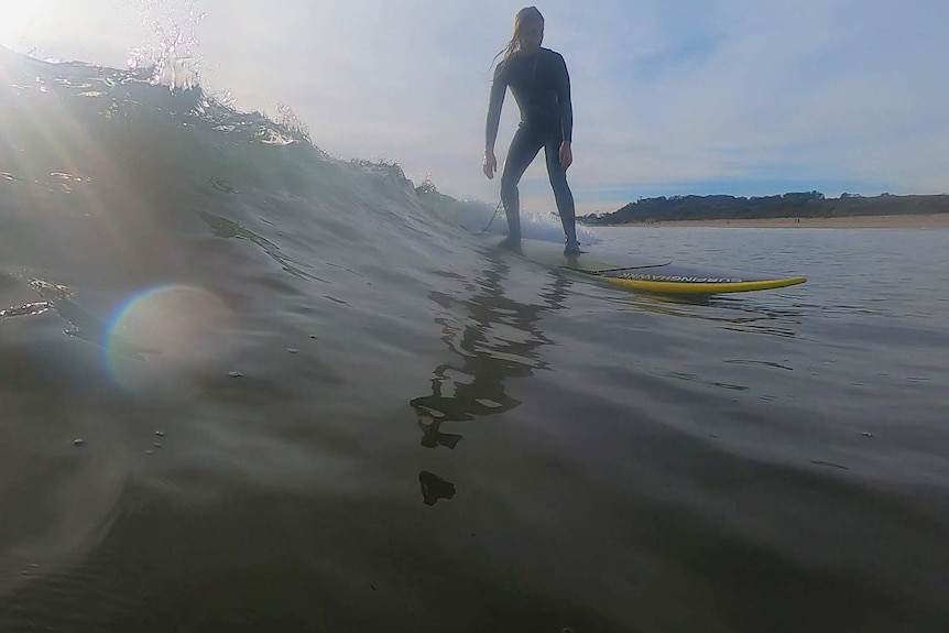 Water shot of a female surfer riding wave towards the water camera.