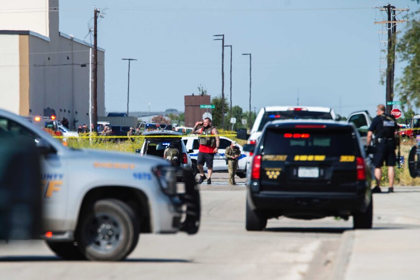 Police vehicles block a road with police tape marking a crime scene in the background