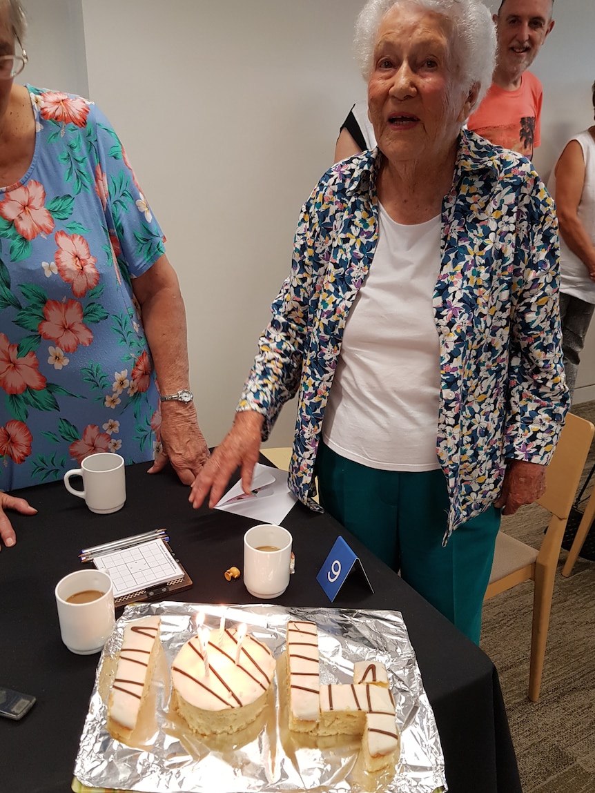 A photo of a woman next to a cake that's made into the shape of "104"