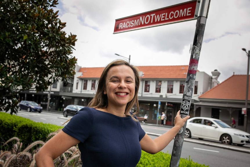 A woman stands below a road sign