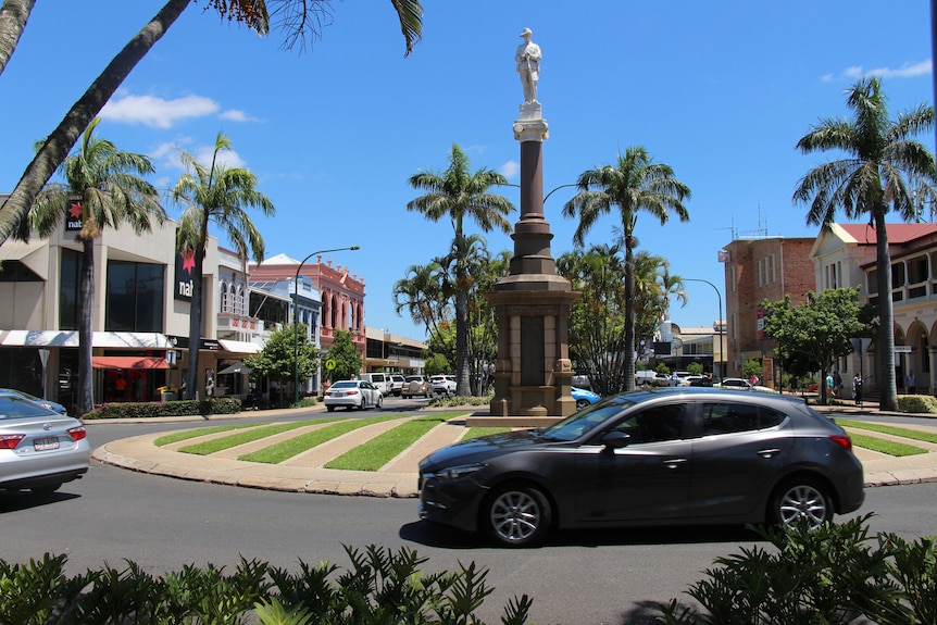 Two cars travelling around a roundabout that has a memorial stature in the middle and grass