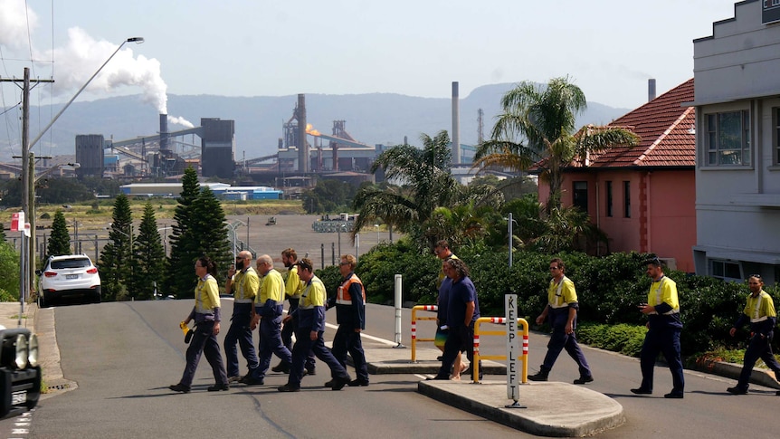 Steelworkers walk across a street in Port Kembla, with the steelworks in the background.