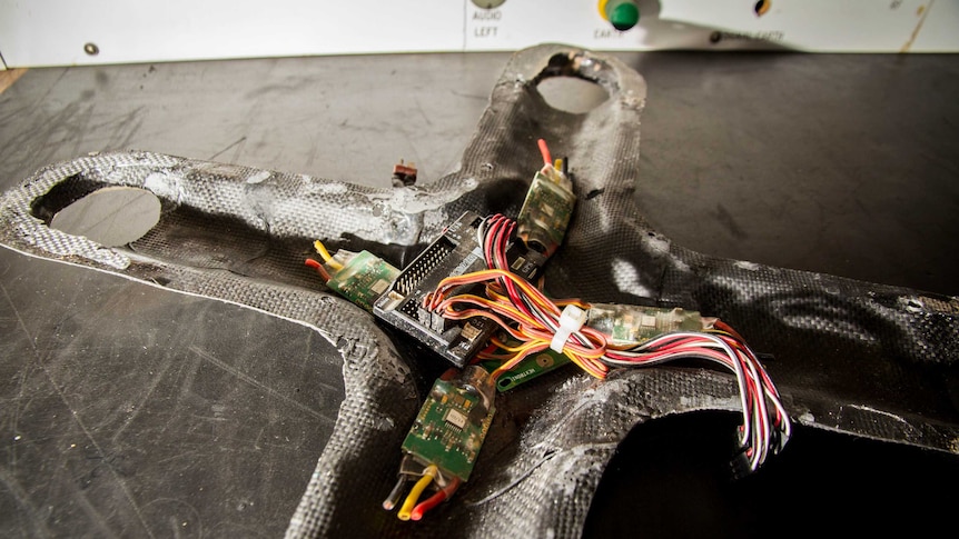 A cross-shaped drone shell sits on a bench.