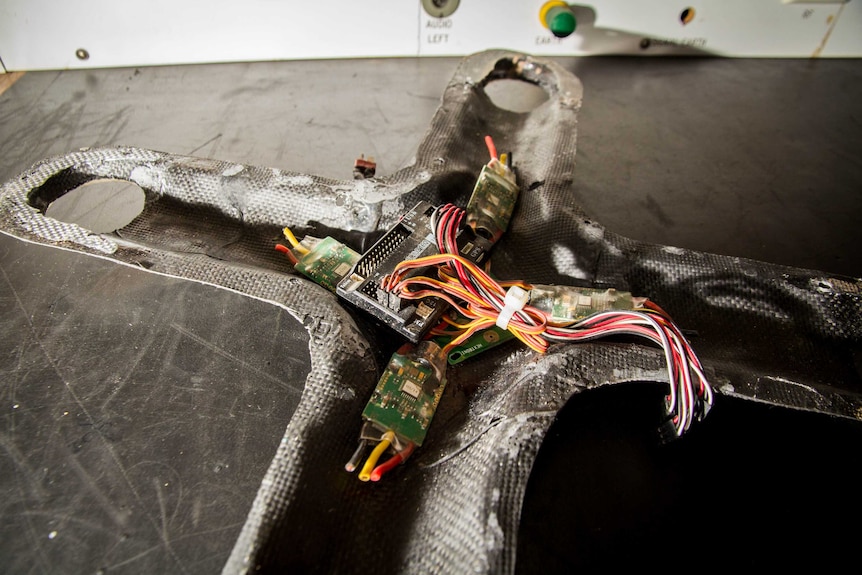 A cross-shaped drone shell sits on a bench.