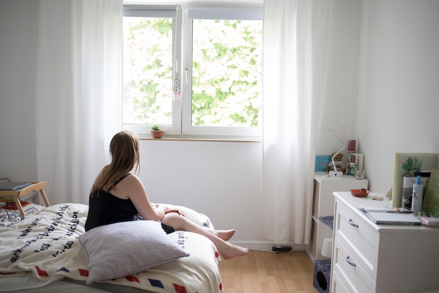 Sofie sits on her bed alone, looking out the window. 