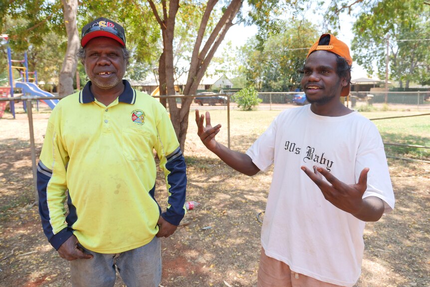 An Indigenous man and a teenager stand next to each other in playground.
