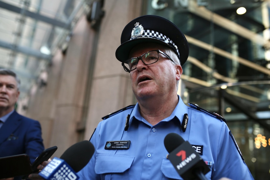 A low angle shot of Police Commissioner Chris Dawson in uniform speaking before microphones outside a CBD building