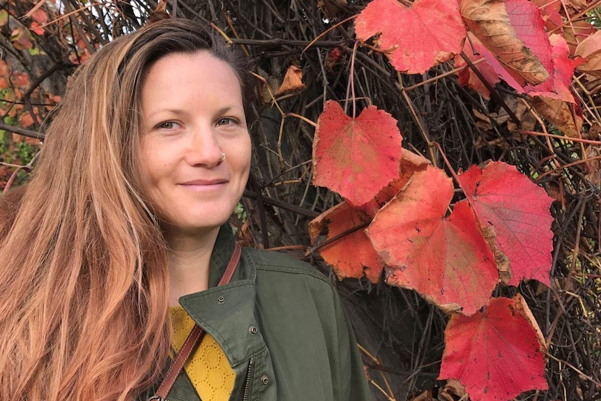 Byron Bay woman Mirabai Nicholson-McKellar poses for a portrait shot in front of a leafy tree.