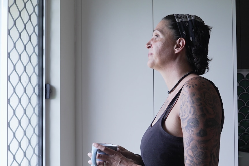 Woman holds cup and looks out window.