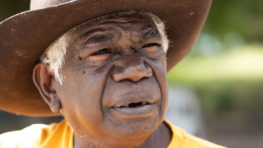 A close-up photo of an Aboriginal man's face. He is wearing a big hat