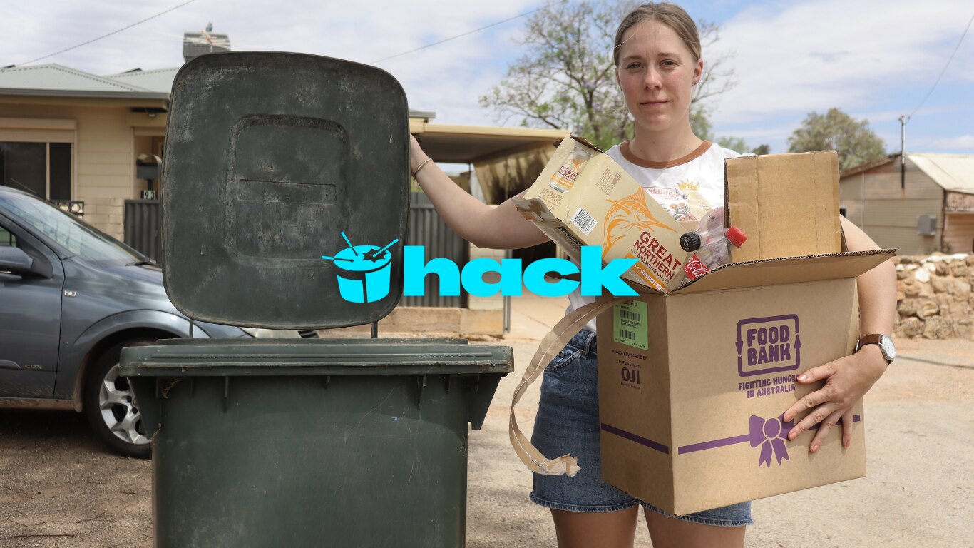 a woman stands next to a general waste bin holding recycling 