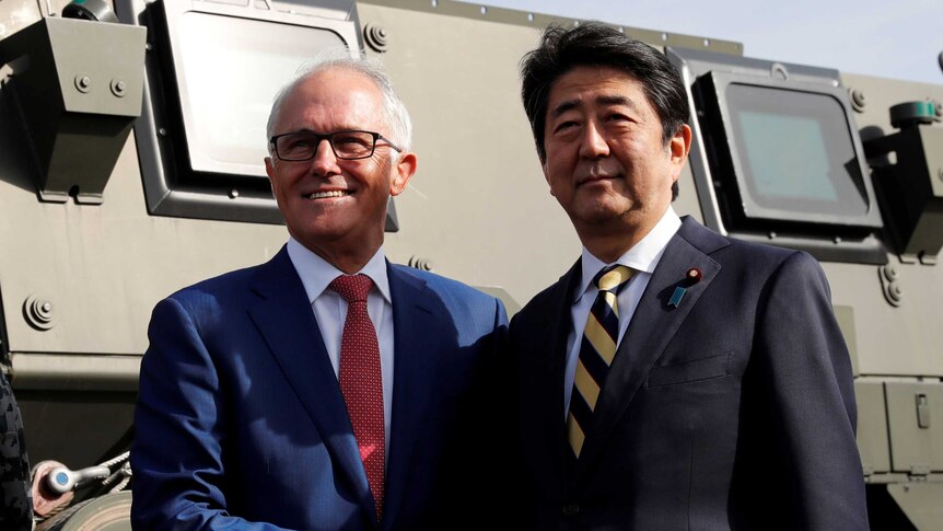 Malcolm Turnbull shakes hands with Shinzo Abe in front of a military vehicle