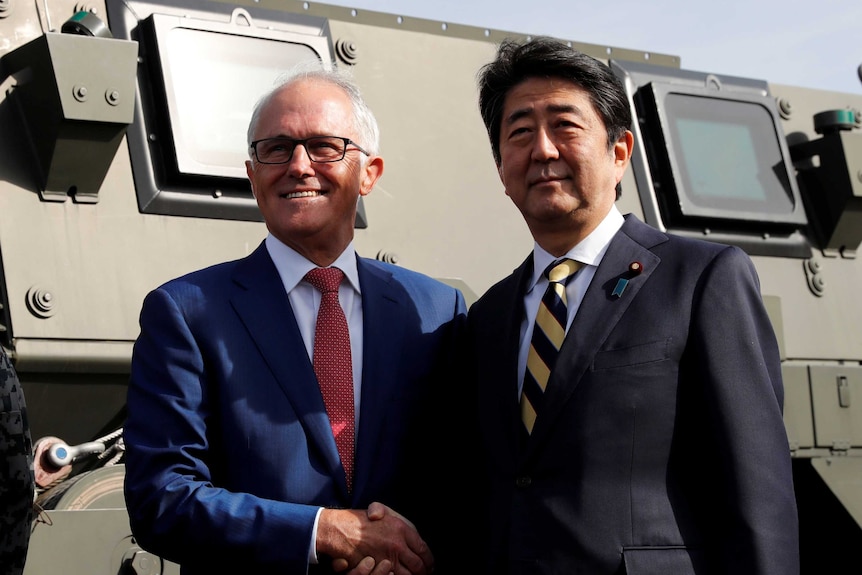 Malcolm Turnbull shakes hands with Shinzo Abe in front of a military vehicle