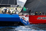 A blue-hulled yacht sails a head of a red-hulled yacht with the crew able to easily see each other.