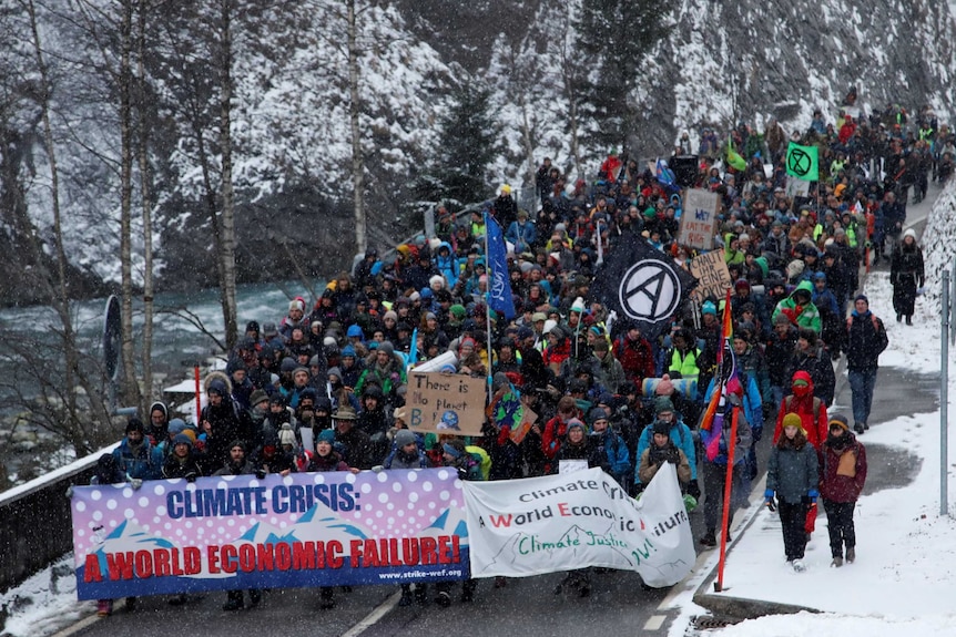 A crowd of people walk through the snow carrying signs during a protest about climate change.