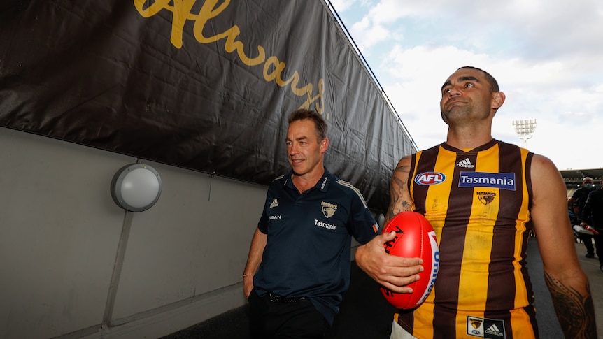 A coach and a veteran player walk down the player's race at the MCG after their final AFL games for Hawthorn.