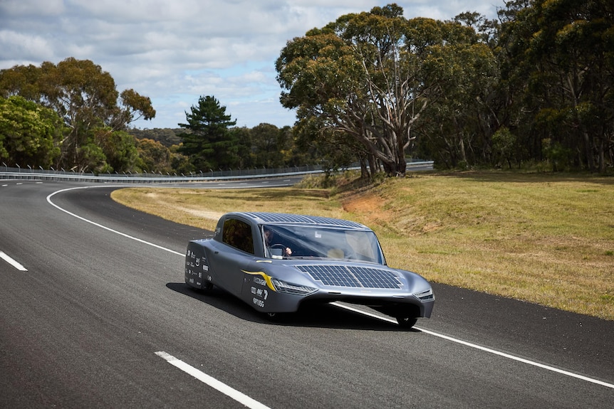 A solar powered car drives on a rural road. 