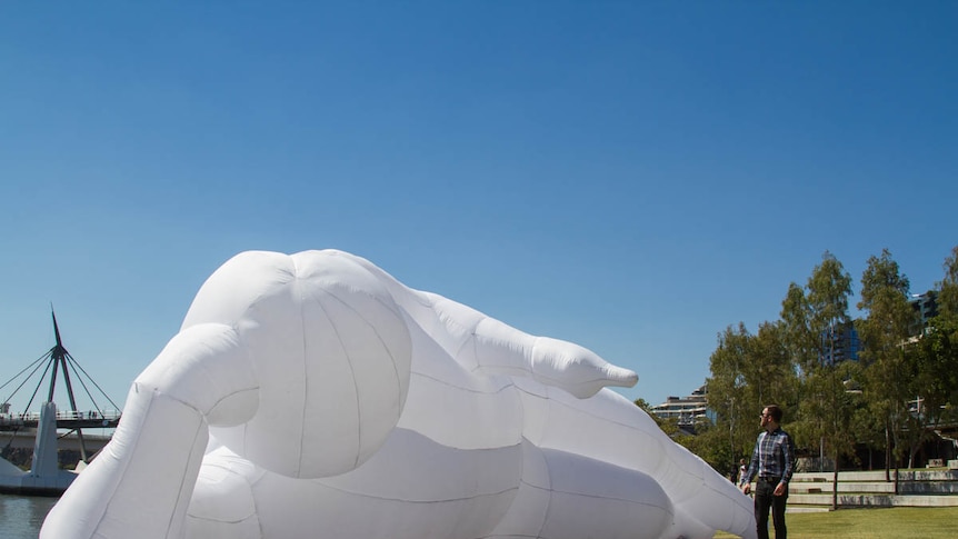 Large white statue sits by the river in Brisbane with a passer-by.