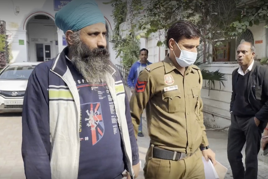 Rajwinder Singh walks into court holding hands with a security guard.