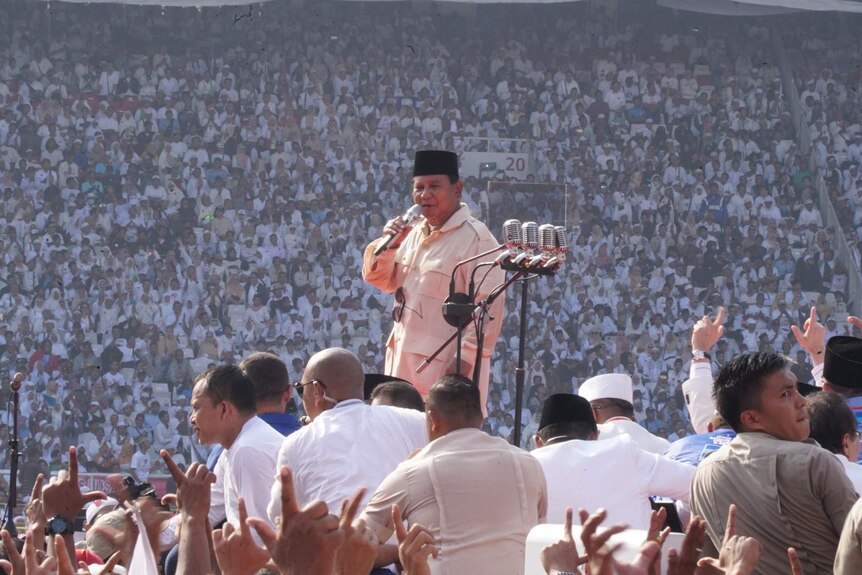 Subianto standing on stage with huge crowd of people in background dressed in white.