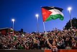A woman waves a national flag in front of a crowd of people waving the same flag after a football game