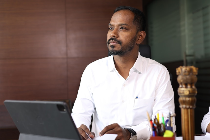 A young Indian man with a beard sits at a computer looking thoughtful 