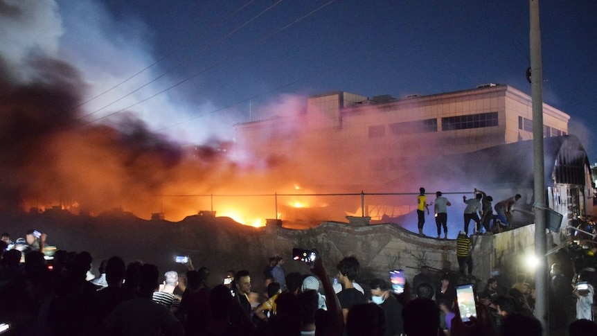 Plumes of smoke rise above a burning hospital building as many watch on