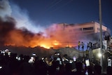 Plumes of smoke rise above a burning hospital building as many watch on