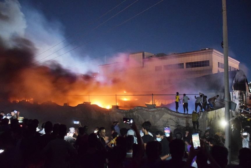 Plumes of smoke rise above a burning hospital building as many watch on