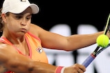 Ashleigh Barty plays a backhand shot, wearing a orange top and a white cap