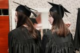 Two women in black graduation gowns and hats look over their shoulder.
