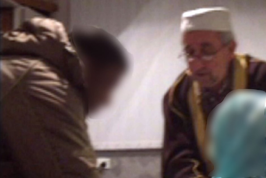 A man in his 30's signs wedding documents while Imam Ibrahim Omerdic looks on.