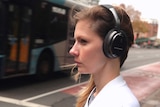 A woman stands next to a busy street while wearing headphones.