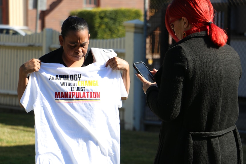 A woman looks down at a white t-shirt she is holding over her torso
