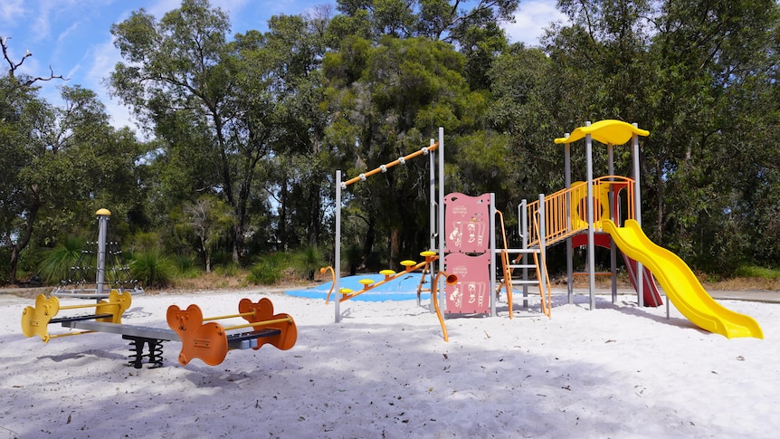 Park with a playground featuring sandpit, seesaw and yellow slide surrounded by tall trees