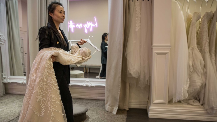 Amelia carries a lace dress across her shop floor