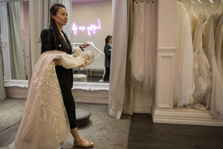 Amelia carries a lace dress across her shop floor