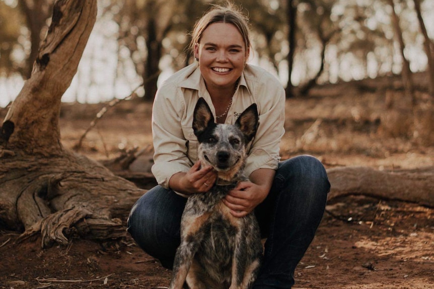 A woman squatting and holdiing a working dog in a rural landscape