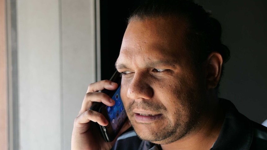 CAAMA Station Manager Gilmore Johnston wearing a blue shirt talking on iPhone