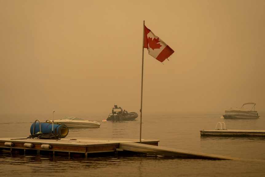 A flag with a maple leaf flaps in the wind as it is surrounded by smoke.