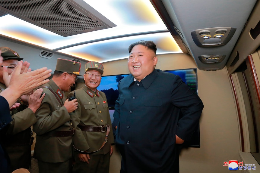 Kim Jong-un in front of a screen laughing while military leaders clap and laugh.