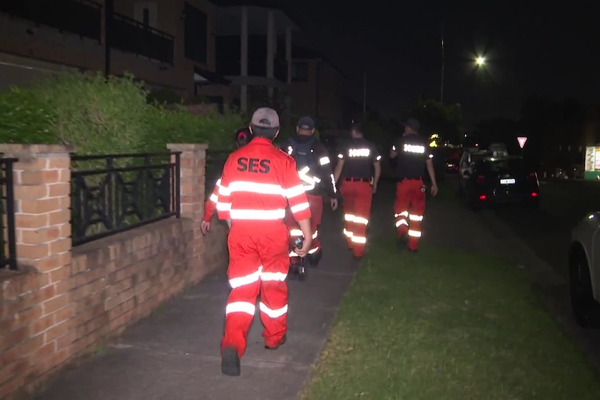 SES crew in reflective clothing walks on suburban footpath at night.