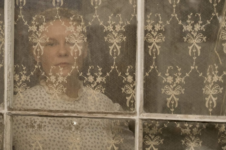 Still image of Kirsten Dunst looking through a curtained window in feature film The Beguiled.