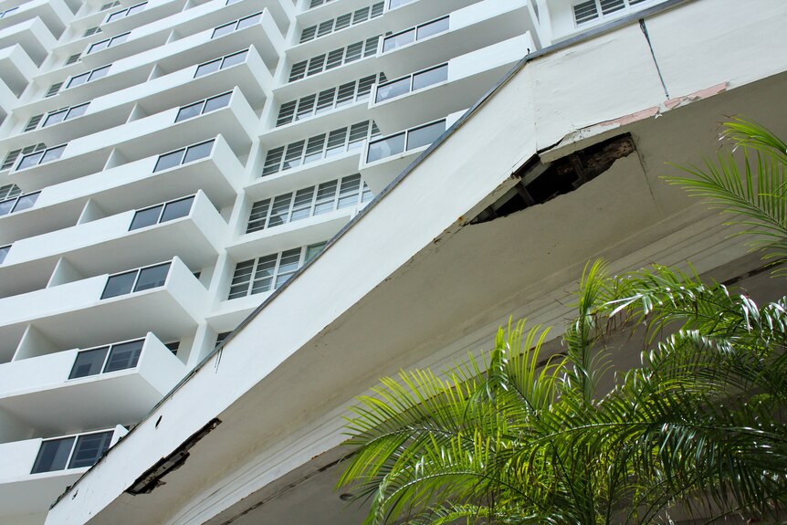 An awning below a highrise apartment building shows cracks in the cement