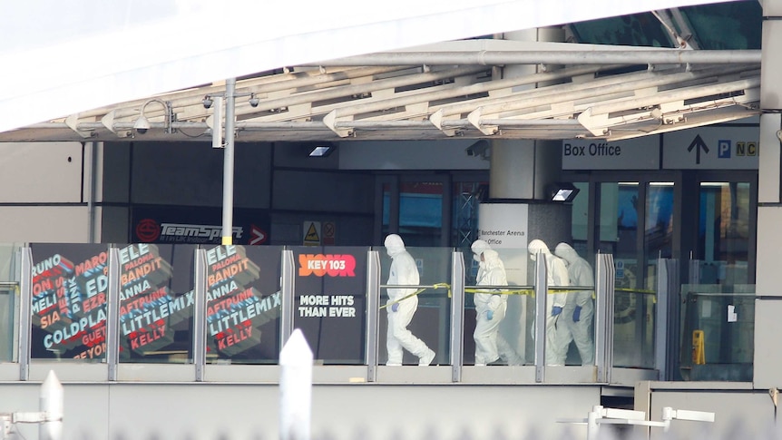 Four police wearing white hazmat suits and masks walk out of the arena.