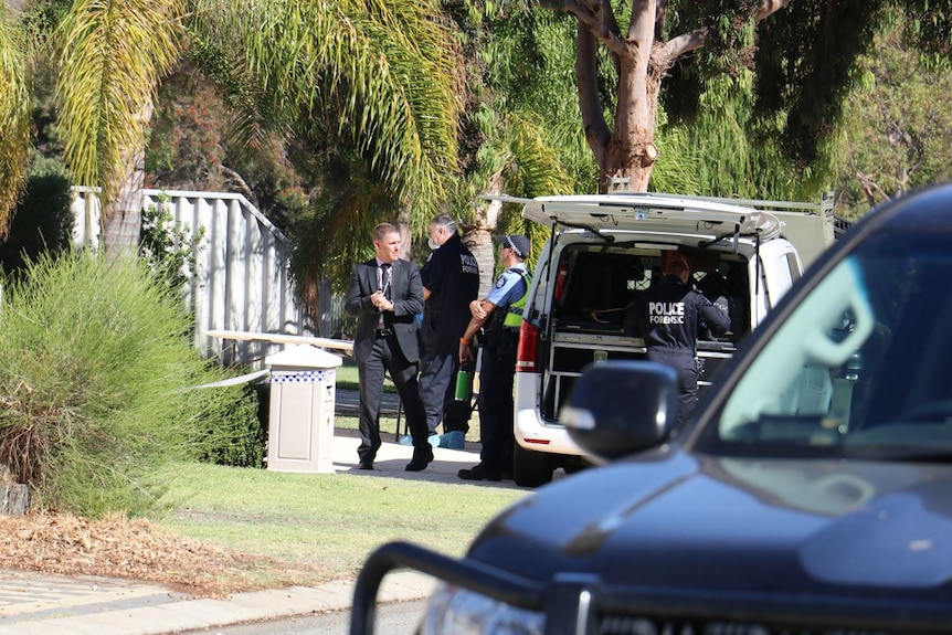 Uniformed and plain clothes police officers gather next to a vehicle parked outside a suburban home.