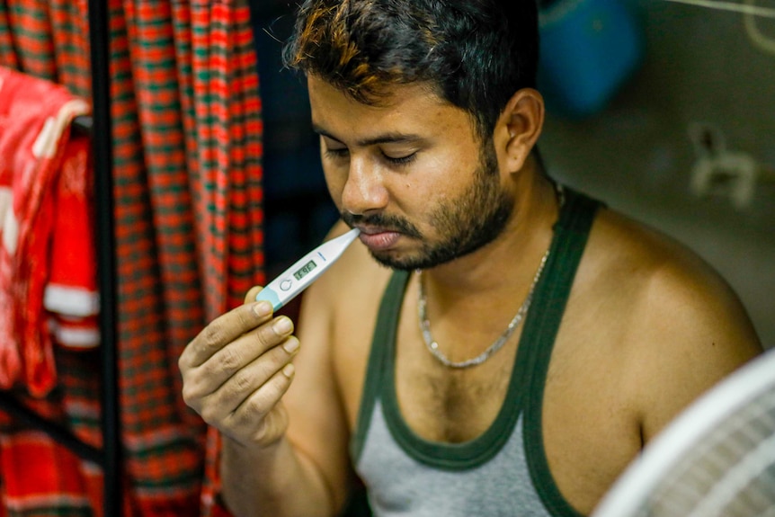 A man in a singlet holds a thermometer in his mouth